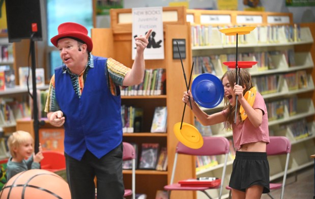 Gregory May playfully knocks spinning plates away from the control of volunteer 9-year-old Tatum Westfall of Hampstead, part of his Circus Science act at the North Carroll Branch library on Thursday. May, a Columbia resident, combines science and circus tricks to educate and entertain her audiences through the background of a former Ringling Brothers circus performer Barnum and Bailey, a science teacher in Baltimore City and an instructor at Port Discovery. (Brian Krista/staff photo)