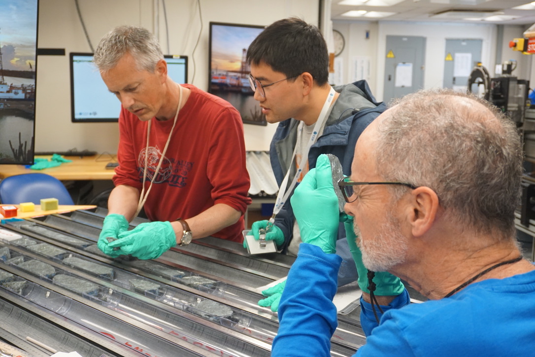 three scientists in a laboratory analyzing a blue core taken from the earth's mantle